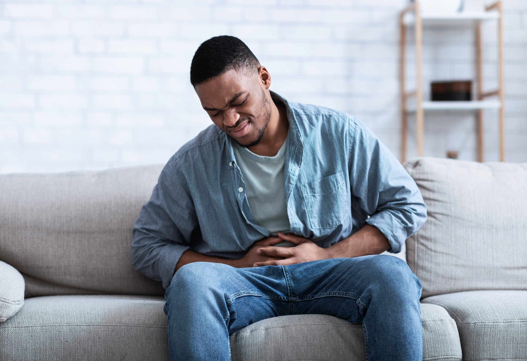 Black Guy Having Painful Stomachache Touching Aching Stomach Sitting Indoors
