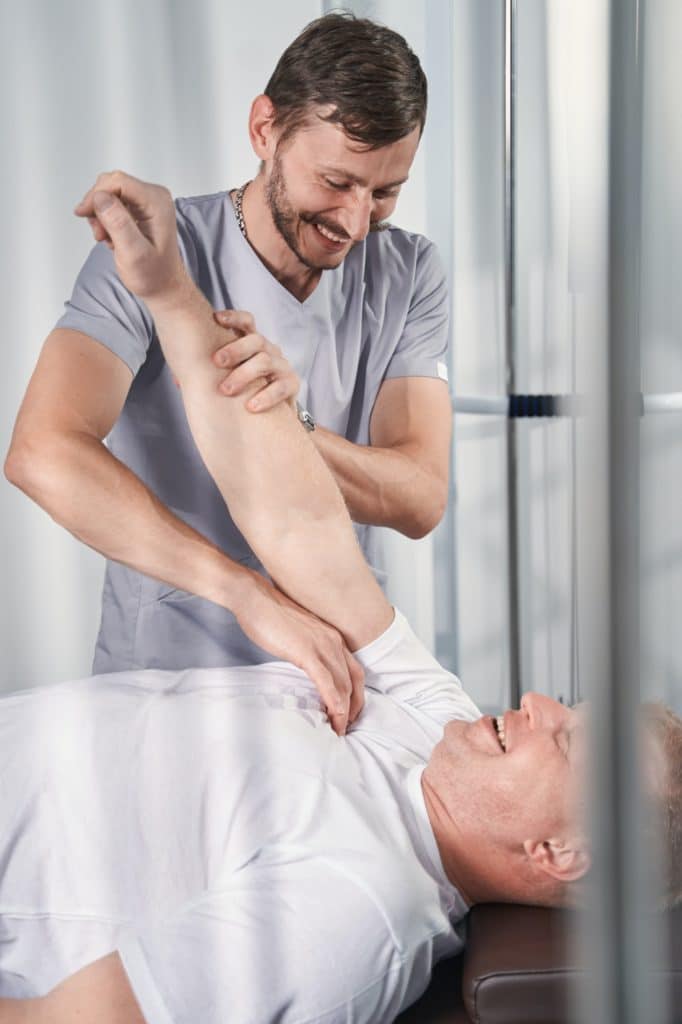Chiropractor checks arm muscles, joints of patient on massage bed